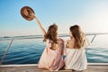 Back portrait of two female friends sitting on boat, waving with hat while talking and enjoying looking at seaside Royalty Free Stock Photo