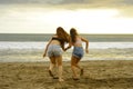 Back portrait of two happy and attractive young women girlfriends holding hands on the beach running to the sea under beautiful su Royalty Free Stock Photo