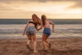 Back portrait of two happy and attractive young women girlfriends holding hands on the beach running to the sea under beautiful su Royalty Free Stock Photo