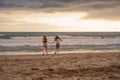 Back portrait of two happy and attractive young women girlfriends holding hands on the beach running to the sea under beautiful su Royalty Free Stock Photo