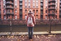 Back rear view of adult woman tourist with white backpack against beautiful historic Speicherstadt warehouse building of