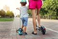 Back rear view of cute little baby boy with young adult mother riding scooter transport on city street park together on