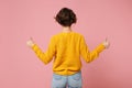 Back rear view of young brunette woman girl in yellow sweater posing isolated on pink wall background studio portrait