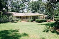 Back Rearview of exterior white cream brick 1950`s house with black shutters and a large lawn lot