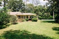 Back Rearview of exterior white cream brick 1950`s house with black shutters and a large lawn lot