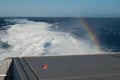 Back of a ship, wake and rainbow.