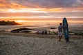 Back shot of an adult man standing on a sandy beach holding surfboard watching the sunset Royalty Free Stock Photo