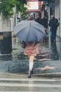 Back shot of a Fashionable young woman walking down a wet street with an umbrella