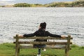 Back shot of a young brown-haired Caucasian woman sitting on a wooden bench, looking relaxed at the sea in Kyleakin Bay on the Royalty Free Stock Photo