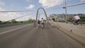 Back side of cycling group of people across bridge in summer cloudness day.