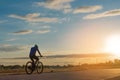 The back side of cyclist rides bicycle on sunset time background.