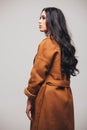 Back side of fashion studio photo of gorgeous sensual woman with dark straight hair wears elegant brown coat