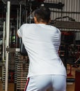 Back side of a gym athlete wearing a white blank shirt pulling the cable rope at a gym Royalty Free Stock Photo