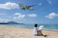 Back side of woman sitting on the beach and looked map, Background at the flying plane above the sea.