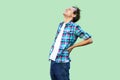 Back or spine pain. Profile side view portrait of tired young man in casual blue checkered shirt and headband standing and holding Royalty Free Stock Photo