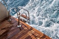 Back teak wooden deck and metal ladder of a of motor yacht, waves and sea splashes and foam Royalty Free Stock Photo