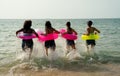 Back of teen girls with swimming rings run in the sea with warm light of sunset during holiday or relax time of vacation at beach Royalty Free Stock Photo