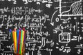 Back to school background with colorful felt pens and blurred math formulas written by white chalk on the black school chalkboard. Royalty Free Stock Photo