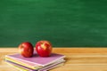 Two red apples and a stack of bright notebooks on a wooden table against the background of a green school board Royalty Free Stock Photo