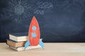 Back to school banner. Painted cardboard rocket next to books in front of classroom blackboard.