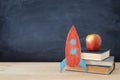 Back to school banner. Painted cardboard rocket next to books in front of classroom blackboard.