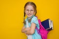 Back to school. Beautiful little girl in glasses and with pigtails with books in a school backpack smiling looking at Royalty Free Stock Photo