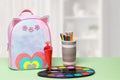 Back to school. A colourful school backpack, pencils or wooden crayons and watercolor paints on a green table over abstract Royalty Free Stock Photo