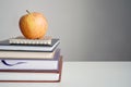 Back to school concept. Apple on books on white table, gray background.