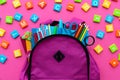 Back to school concept. Backpack with school supplies and alphabets and numbers blocks on pink background. Top view. Copy space