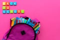 Back to school concept. Backpack with school supplies and alphabets and numbers blocks on pink background. Top view. Copy space