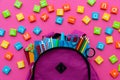Back to school concept. Backpack with school supplies and alphabets and numbers blocks on pink background. Top view. Copy space