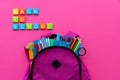 Back to school concept. Backpack with school supplies and alphabets and numbers blocks on pink background. Top view. Copy space