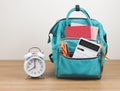 Front view of green backpack with school supplies and alarm clock 8 o\'clock on wooden table and white background Royalty Free Stock Photo