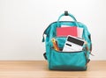 Front view of green backpack with school supplies on wooden table and white background with copy space Royalty Free Stock Photo