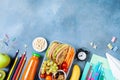 Back to school concept. Healthy lunch box and colorful stationery on blue table top view.