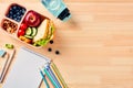 Back to school concept. Lunch box with healthy food, paper notebook, colorful school supplies on wooden table. Top view, flat lay Royalty Free Stock Photo