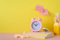 Back to school concept. Photo of school supplies on pink table alarm clock stand for pens stack of notebooks pencils mini stapler Royalty Free Stock Photo