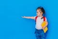 Back to school concept. School girl with red backpack and holding yellow folder in front of blue background. The child