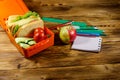 Back to school concept. School supplies, apple and lunch box with sandwiches and fresh vegetables on wooden desk