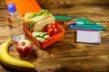 Back to school concept. School supplies, bottle of water, apple, banana and lunch box with sandwiches and fresh vegetables