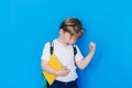 Back to school concept. Schoolboy boy with backpack and holding yellow book in front of blue background. Child clenched Royalty Free Stock Photo