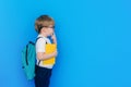 Back to school concept. Schoolboy boy with backpack and holding yellow notebook in front of blue background. Child Royalty Free Stock Photo