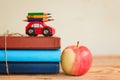 Back to school concept with stack of books and red apple and miniature car carrying colorful pencil.