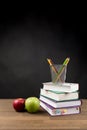 Back to School Concept, Stacked books, Coloring Pencils and red and green apple isolated on black blackboard background Royalty Free Stock Photo