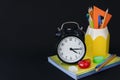 back to school concept. School supplies, stack of notebooks and round clock are on black background. Royalty Free Stock Photo