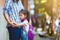 Cute asian pupil girl with backpack hugging her mother with sadness before go to classroom in the school