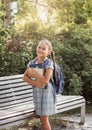 Back to school. A cute little schoolgirl in a dress with pigtails and large blue backpackis holds books and stand in the school