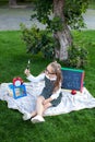 Back to school. Cute smiling schoolgirl in glasses sitting on grass with books holds a magnifying glass magnifier in her hands