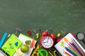 Back to school and education concept with alarm clock, school supplies and fresh green apple on blackboard background top view Royalty Free Stock Photo