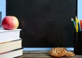 Back to school, education concept. Books, useful whole-grain cookies and apple on classroom table in front of blackboard. Royalty Free Stock Photo